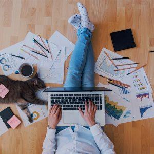 Woman working from home, sitting on the floor with a cat next to her.