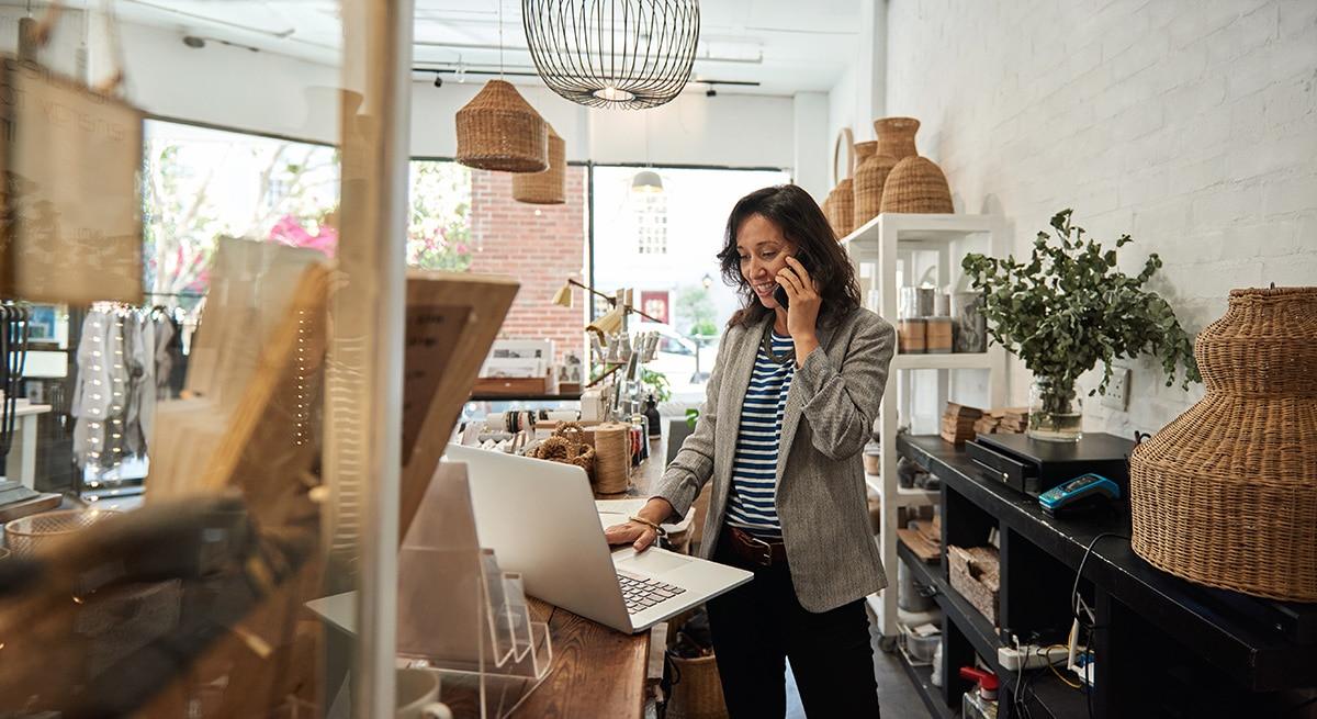 Female small business owner standing in her furniture store, working on a laptop. 